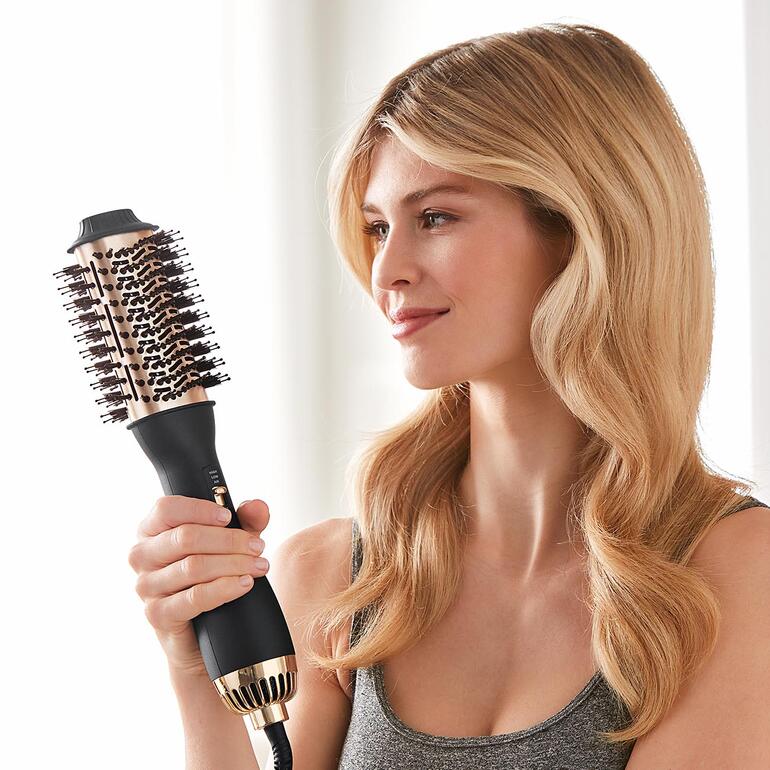 Frau hält eine 4-in-1-Warmluftbürste und lächelt.