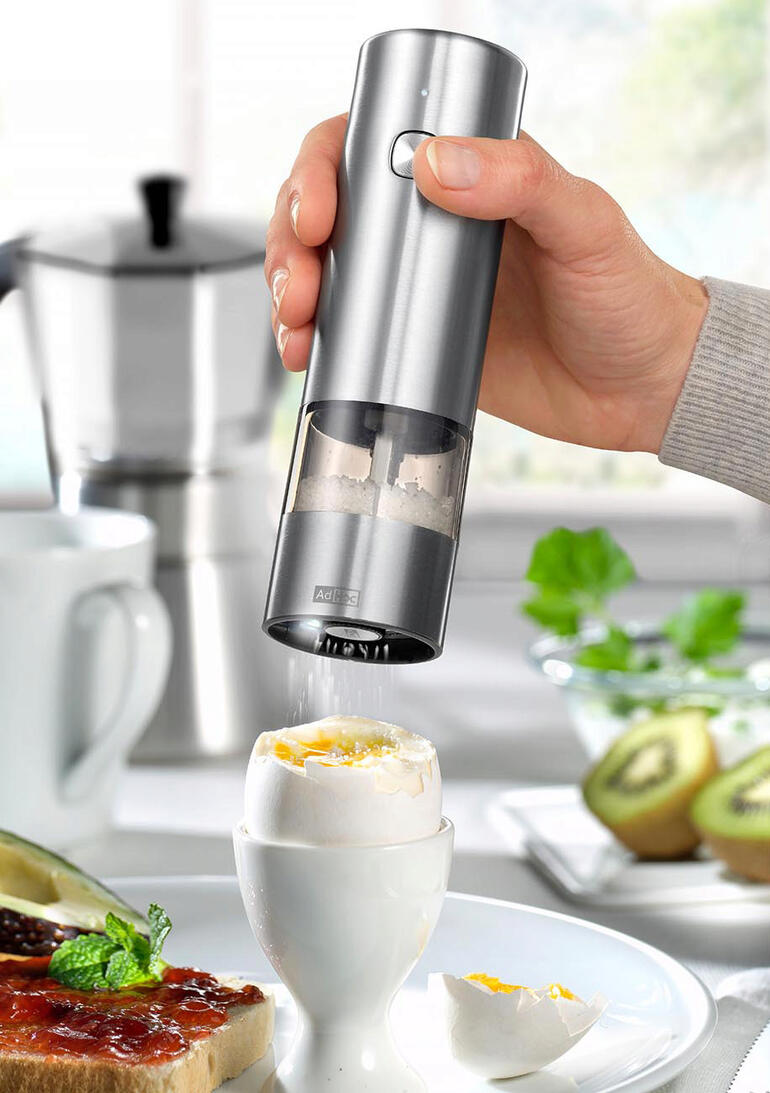 Hand hält eine Akku-Gewürzmühle über ein Ei mit Spitzen.