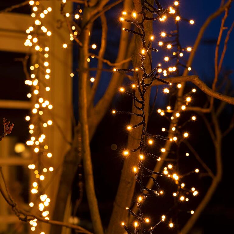 Kaskaden-Lichterkette leuchtet an einem Baum bei Dämmerung