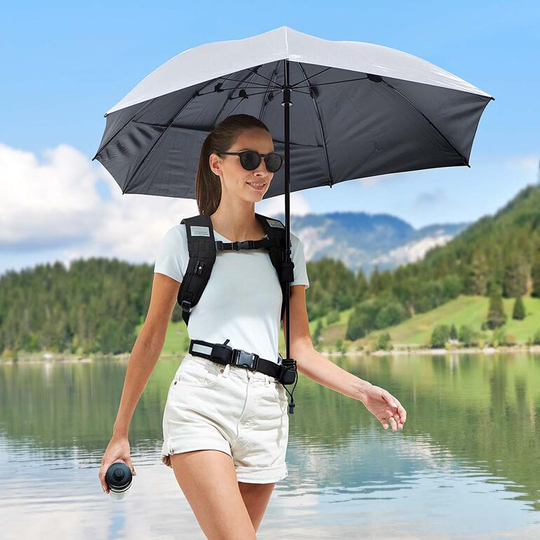 Frau mit freihändigem Rucksackschirm vor einem See.
