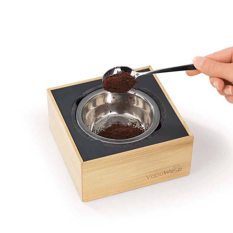 Räucherbox VapoWesp mit einer Hand, die Kaffeepulver einfüllt.