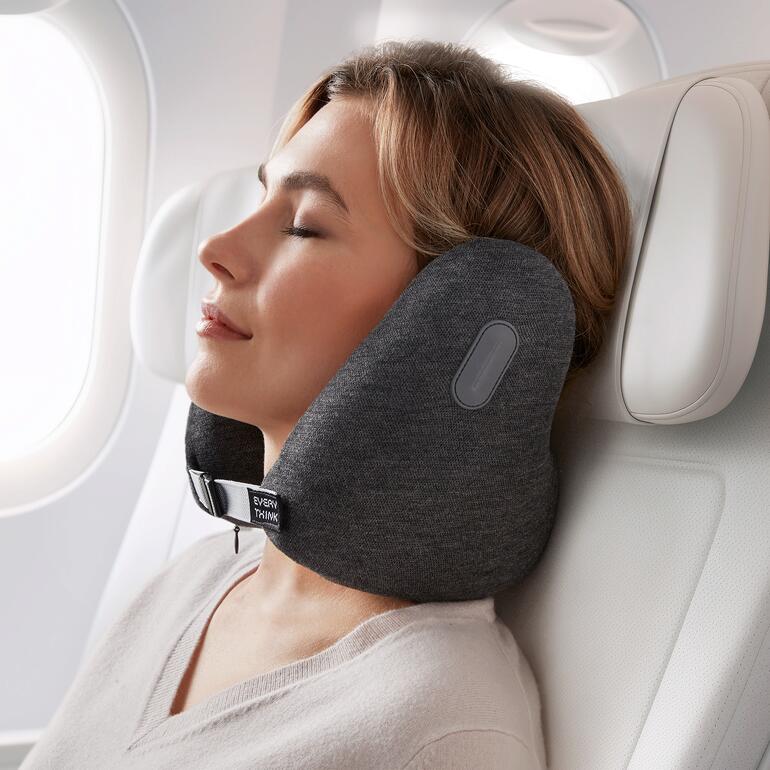 Frau mit Nackenkissen im Flugzeug, Augen entspannt geschlossen.