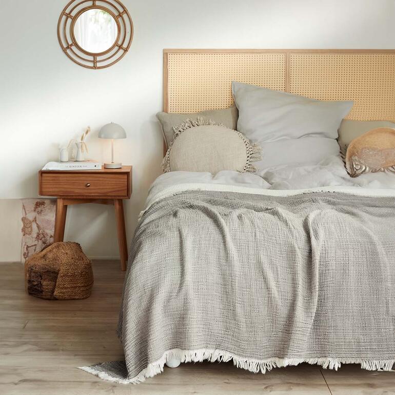 Ideal auch als leichter Bettüberwurf. Musselindecke in grau auf einem Bett mit Kopfteil und Kissen.