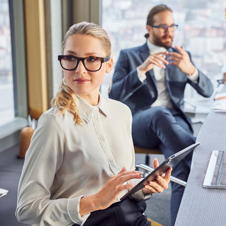Frau mit Audio-Brille in einem modernen Büro, Tablet in der Hand.