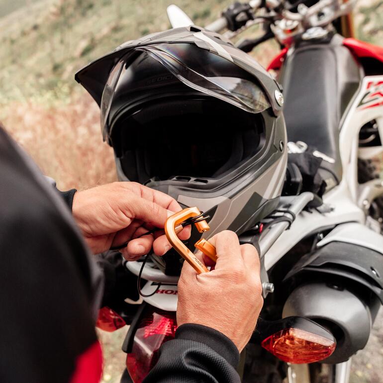 Person befestigt einen Karabinerhaken mit Schloss an einem Motorradhelm.