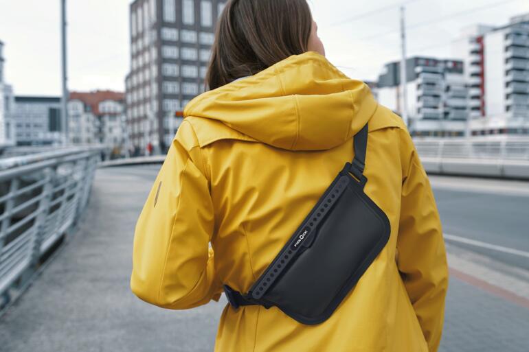 Frau mit gelber Jacke trägt eine schwarze Crossbody-Tasche auf der Schulter.