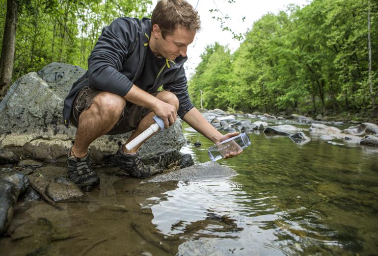 Mann füllt Wasser aus einem Bach mit einer Wasserfilter-Flasche