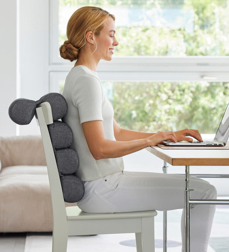 Frau sitzt mit Flexi-Rollenkissen am Schreibtisch und arbeitet am Laptop.