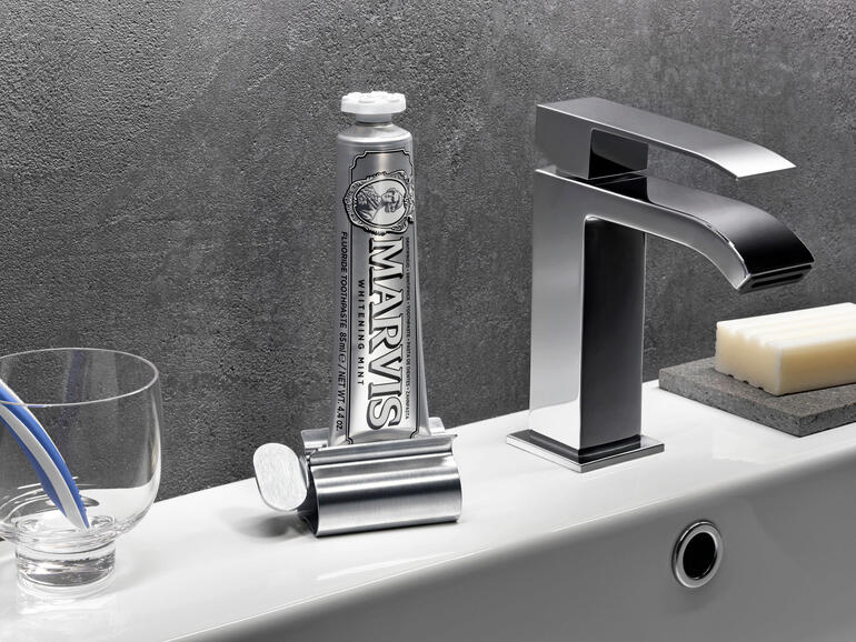 Edelstahl-Tubenpresse mit einer Tube Zahnpasta neben einem Wasserhahn.