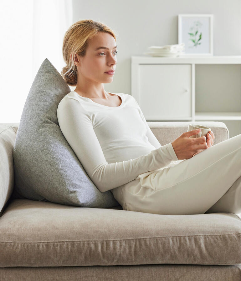 Frau mit einem grauen Rückenkissen, die entspannt auf einer Couch sitzt.