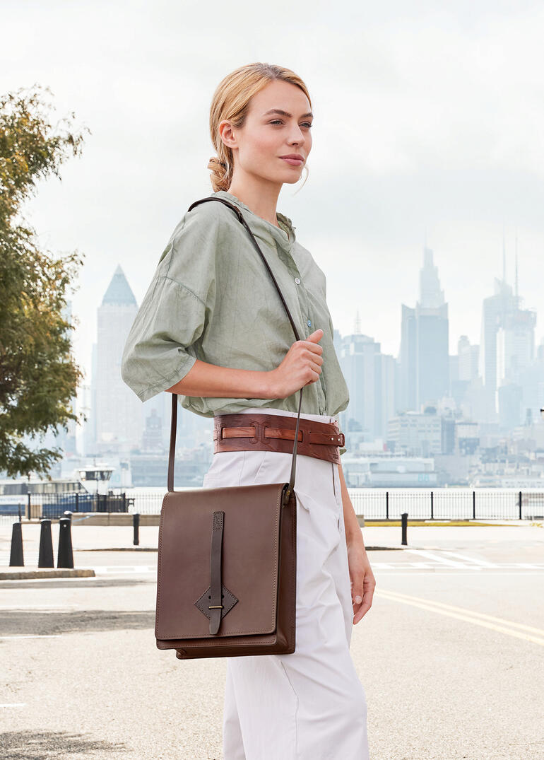 Frau trägt eine braune Chiarugi Kartentasche über der Schulter vor einer Stadtansicht.
