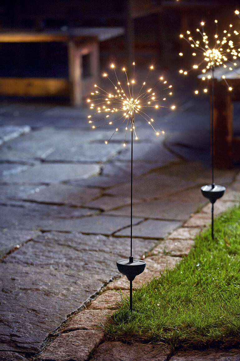 Solar-Wunderkerze leuchtet im Garten auf einem Steinweg.