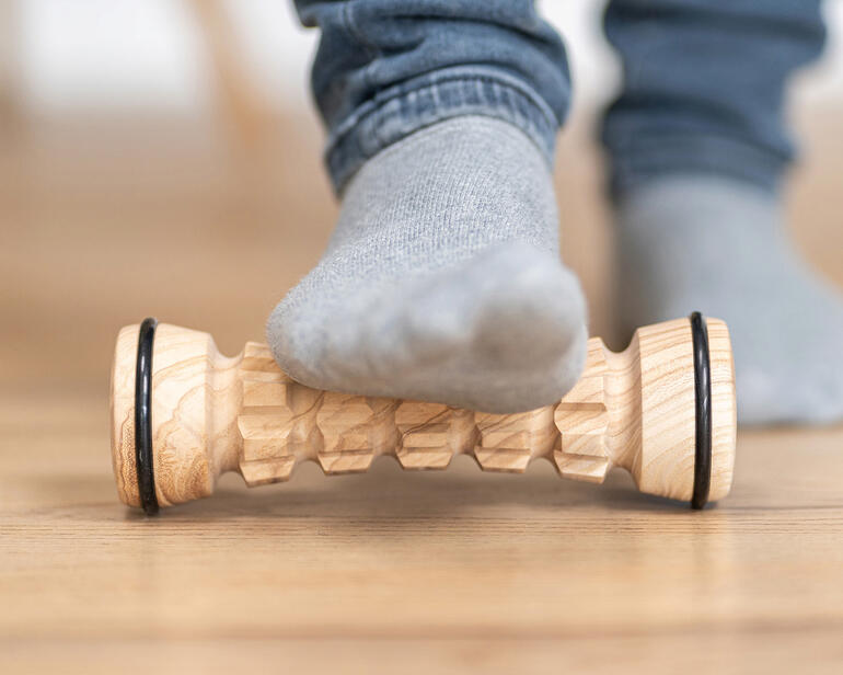 Fußmassage-Roller aus Holz, ein Fuß liegt darauf.