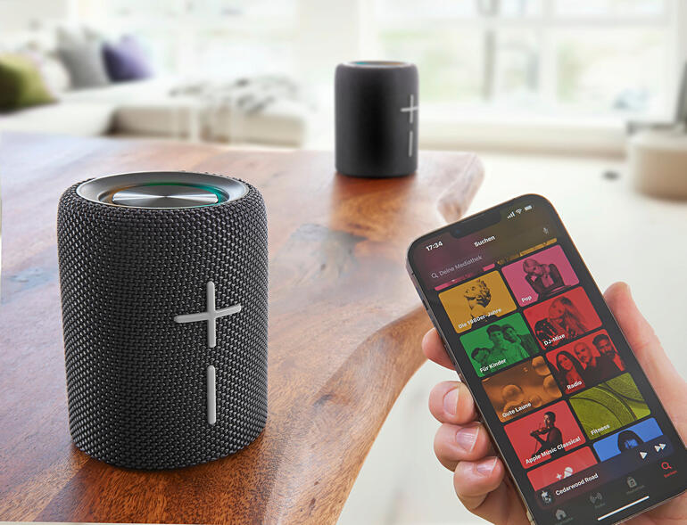 Smartphone zeigt Musik-Streaming-App neben Teilbarem Bluetooth Lautsprecher.