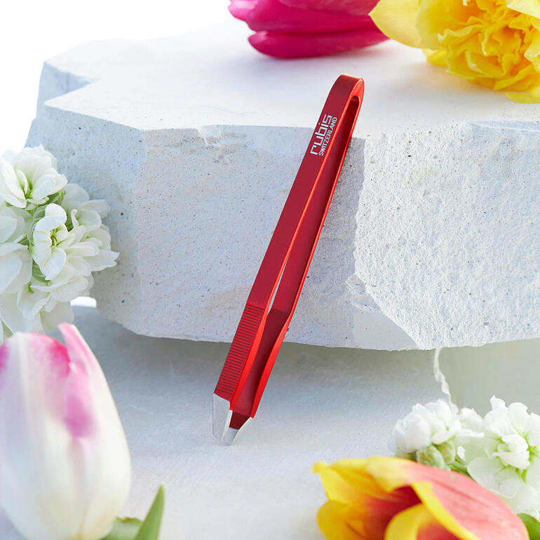 Ultraleichte Pinzette in rot, auf einer weißen Steinoberfläche platziert, umgeben von Blumen.