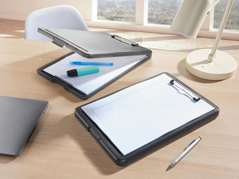 Zwei transparente Clipboard-Ordner auf einem Schreibtisch mit Stiften und Laptop.