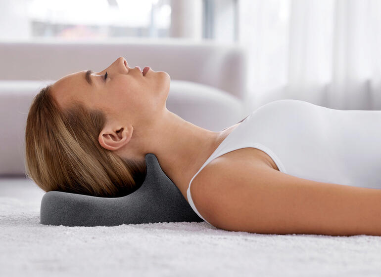 Frau liegt mit Spezial-Nackenstütze auf dem Rücken, entspannt