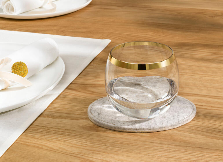 Glas mit Wasser auf einem grauen Filz-Tropfenstopper.