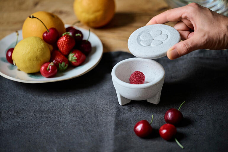 Porzellan-Fruchtfliegenfalle mit einer Hand, die den Deckel öffnet und Obst auf dem Tisch.