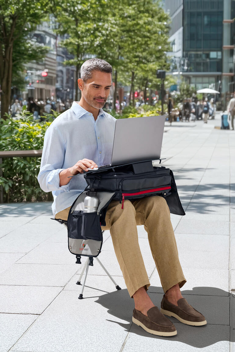 Mann sitzt auf einem Stuhl und arbeitet an einem Laptop, der auf einem mobilen Rucksack-Arbeitsplatz steht.