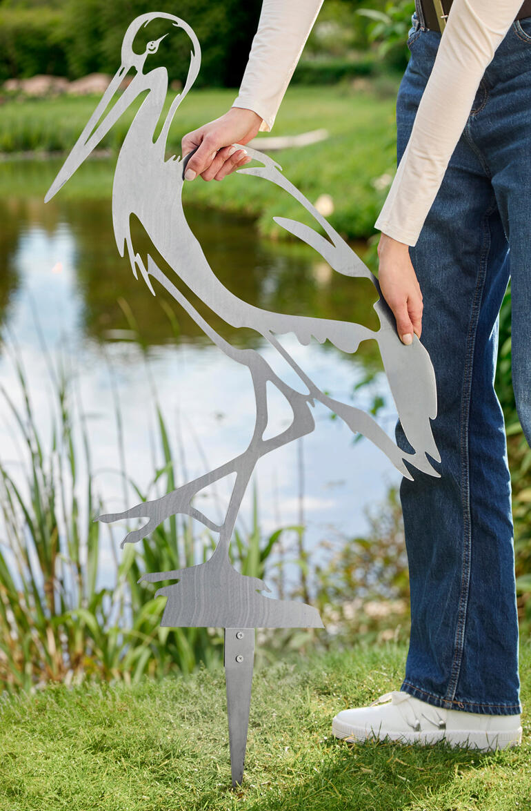 Der 27 cm lange Erdspieß sorgt für eine stabile Verankerung im Boden und zuverlässigen Halt. Person, die einen Gartenstecker in Form eines Storches in den Boden steckt