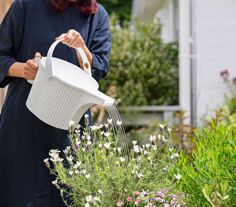 Frau gießt Blumen mit einer Gießkanne im Garten