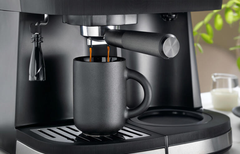 Aromatischer Espresso zu Hause und im Büro – professionell zubereitet wie in der Kaffeebar. Schwarze Tasse wird unter einem Espresso-Auslass positioniert.
