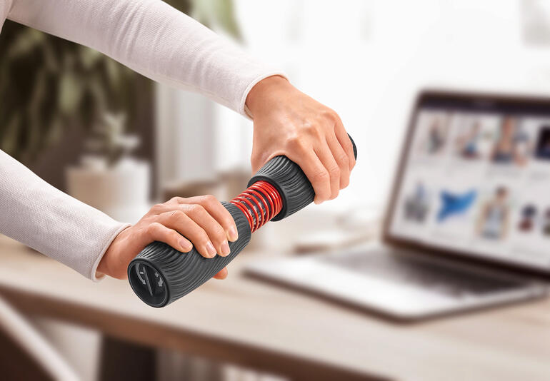 Person trainiert mit Handgelenk- und Unterarmtrainer an einem Tisch mit Laptop.