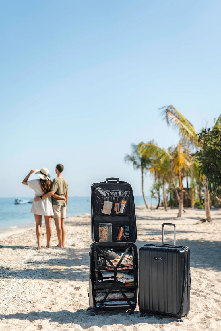 Kofferstapel am Strand mit einem Paar Menschen im Hintergrund.