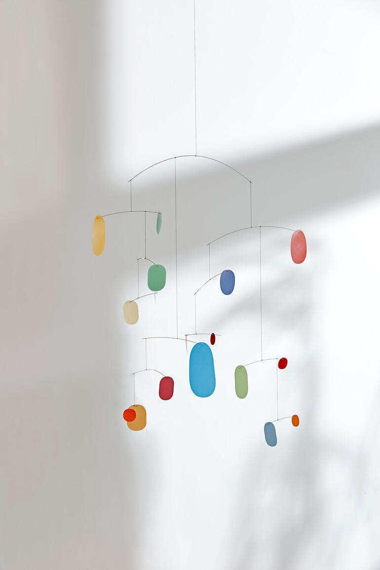 Mobiles Kunstobjekt mit bunten Elementen, schwebend an einem Faden.