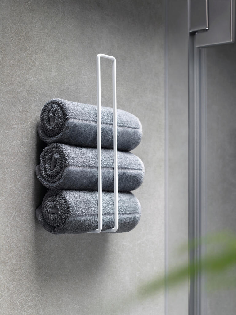 Drei graue Handtücher ordentlich gestapelt in einem weißen Design WC-Rollenhalter.