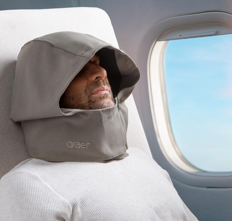Mann mit Reisekissen und Kapuze schläft im Flugzeug.