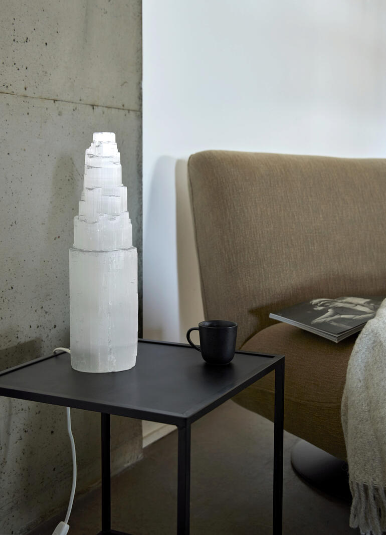 Faszinierend sogar bei ausgeschaltetem Licht. Selenit-Lampe steht auf einem Tisch neben einem Glas.
