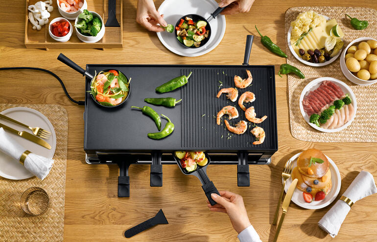 Drehen Sie die Grillplatte um: Schon können Sie Asiatisches aus dem Mini-Wok und Pfannkuchen und Crêpes zubereiten. Solis Raclette- und Fun-Cooking 5-in-1-Gerät wird mit Meeresfrüchten serviert.