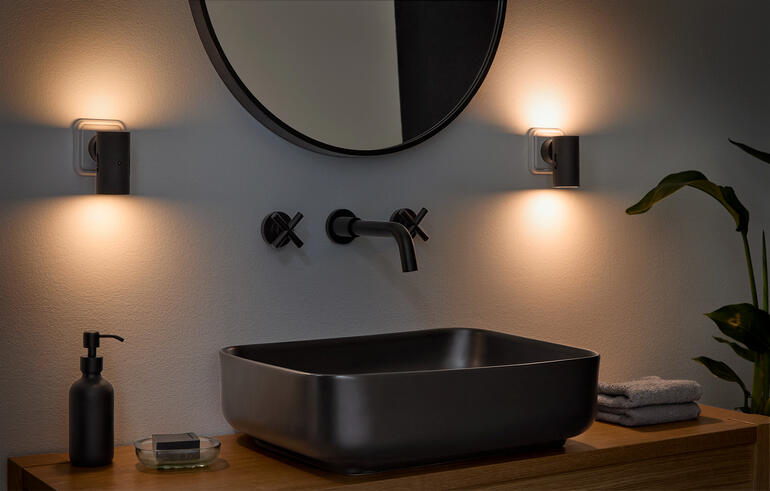 Dimmbare Wandleuchte in einem Badezimmerumfeld neben einem modernen Waschbecken.
