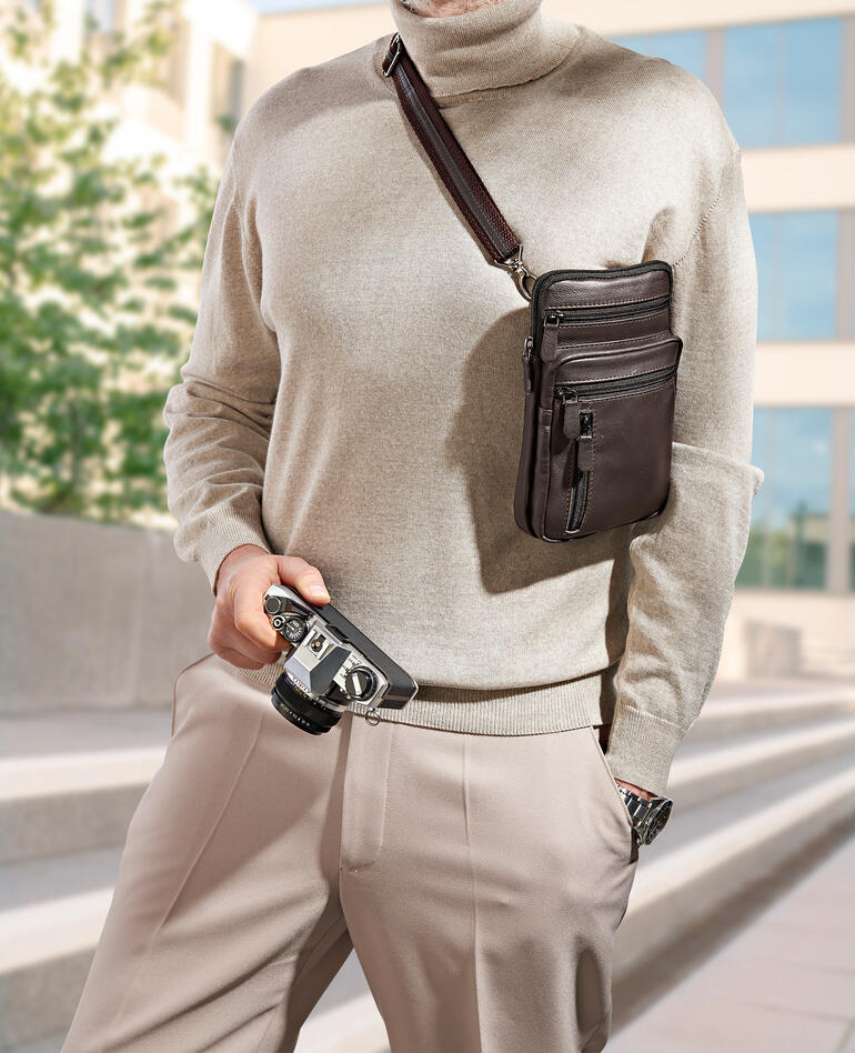 Mann trägt eine Büffelleder-Gürteltasche über der Schulter und hält eine Kamera in der Hand.