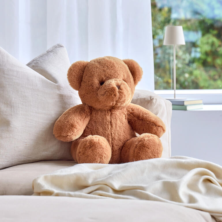 Brauner Teddybär auf einer bequemen Couch, bereit zum Kuscheln.