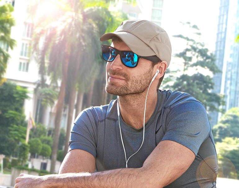 Mann mit beige Kühlkappe und Sonnenbrille sitzt im Freien