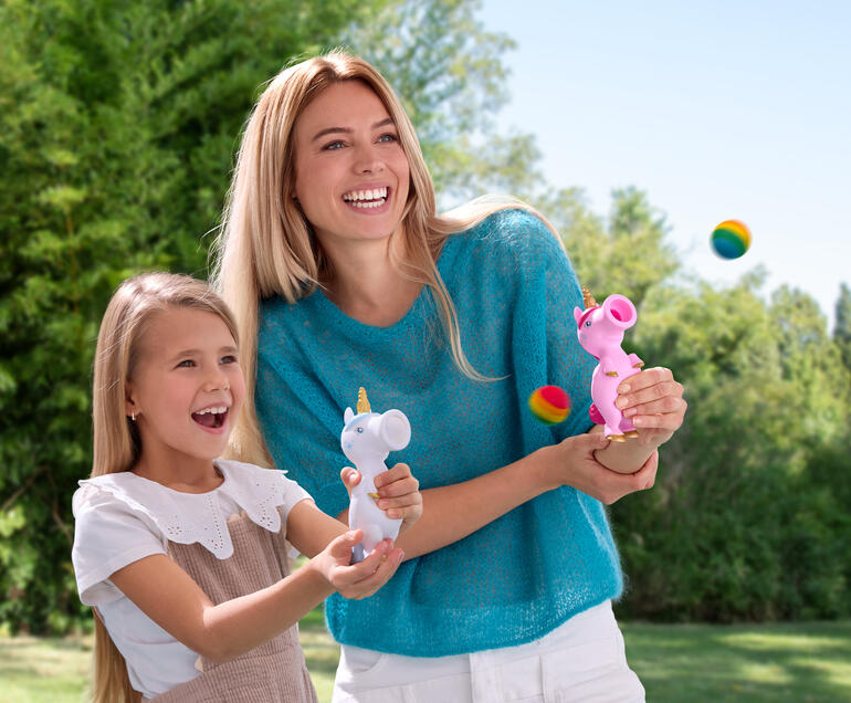 Frau und Mädchen lachen beim Spielen mit Einhorn-Ploppern im Freien.