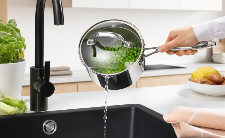 Stielkasserolle mit Siebdeckel, Wasser wird in die Spüle gegossen.