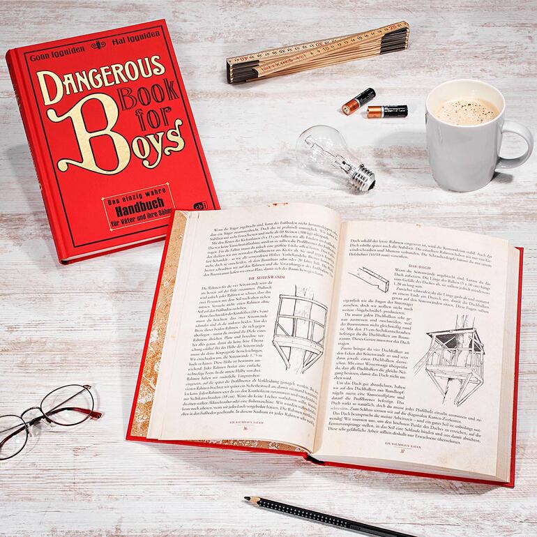 Buch 'Dangerous Book for Boys' auf einem Tisch, offen mit einer Tasse Kaffee.
