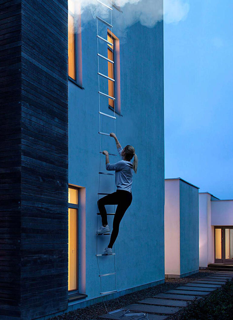 Frau klettert eine Rettungsleiter an der Wand hinauf.