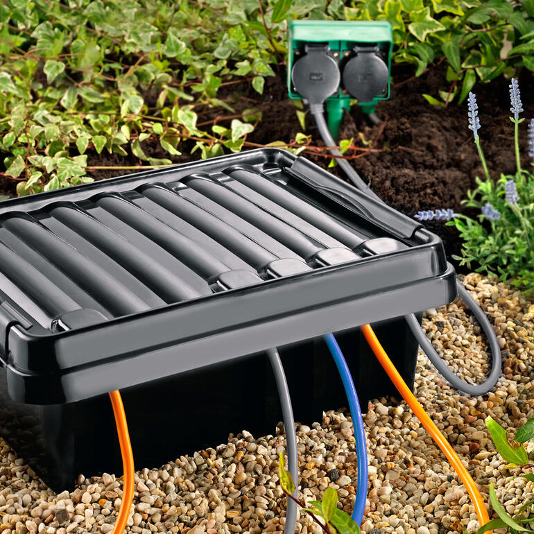 DRi®BOX mit Kabeln auf der Erde, umgeben von Pflanzen.