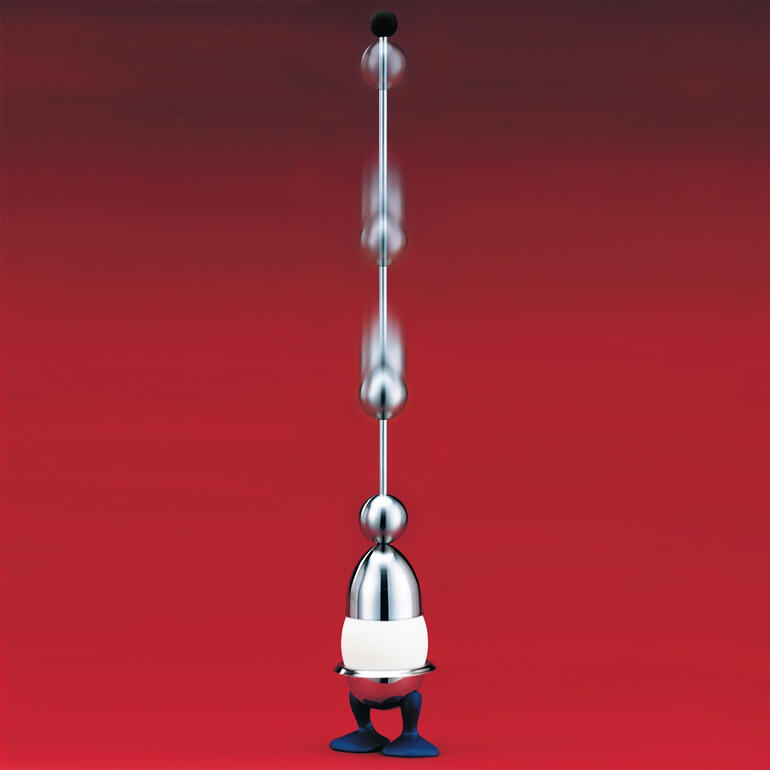 Clack-Eierschalenöffner in glänzendem Metall, auf rotem Hintergrund.