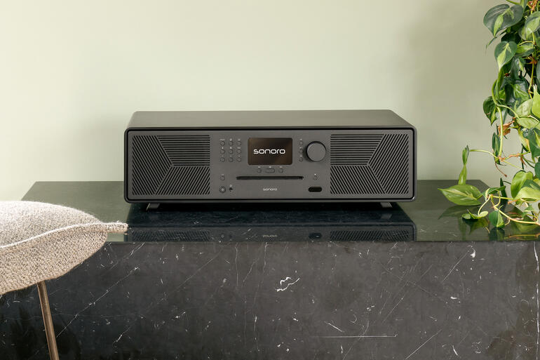 Sonoro Meisterstück Gen. 3 auf einem beigen Tisch mit Pflanzen im Hintergrund.