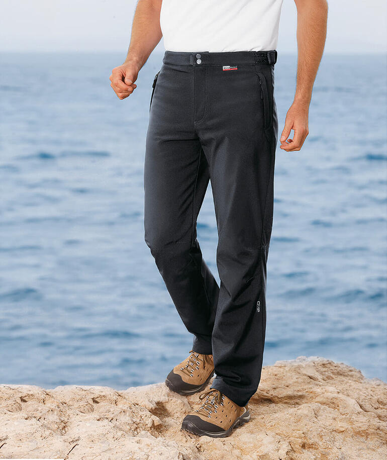 Mann in schwarzen Softshell-Hosen steht am Meer.
