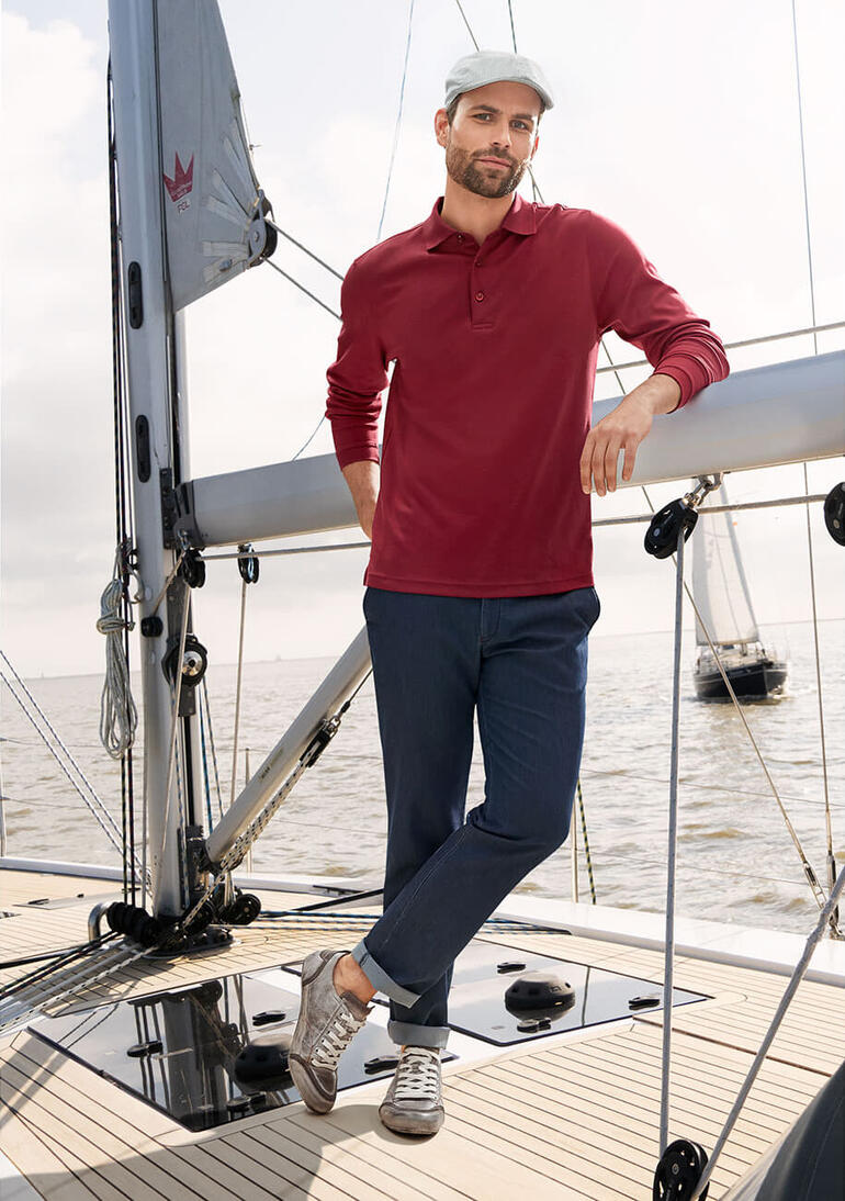 Mann in rotem Pima Interlock Polo Shirt steht auf einem Boot, lächelt.