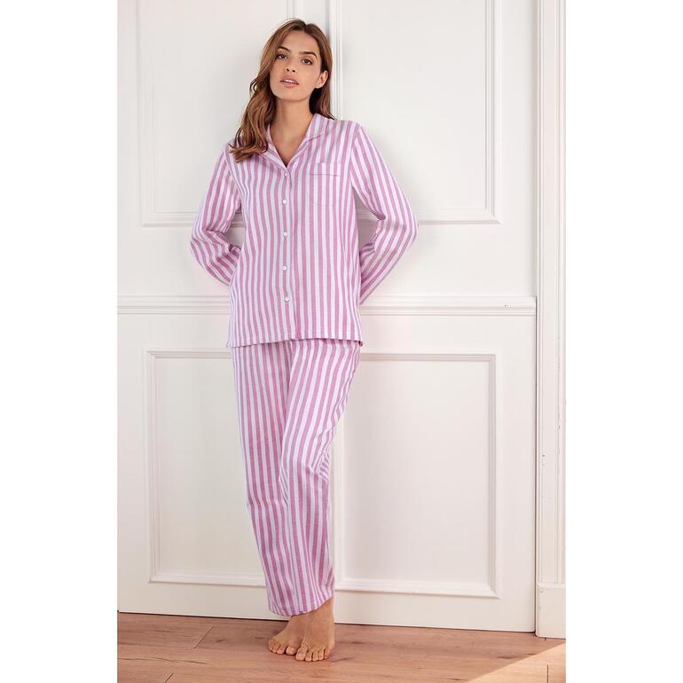 Frau in pinkem gestreiften Flanell-Pyjama leans an einer Wand.