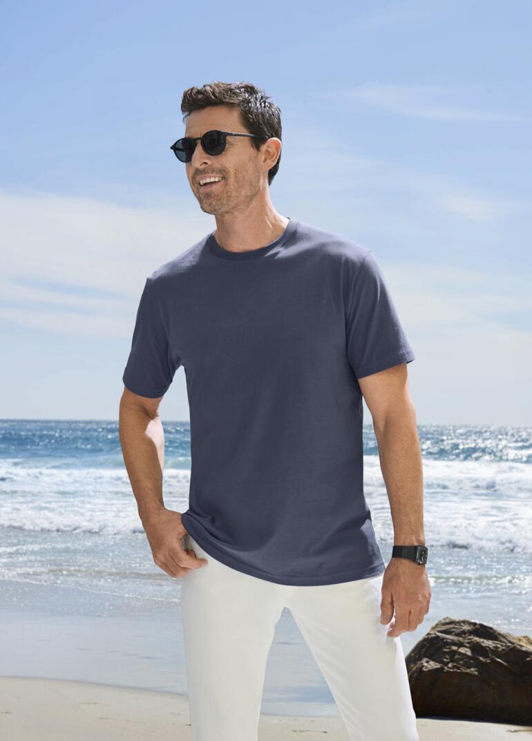 Mann mit blauem T-Shirt und Sonnenbrille am Strand.