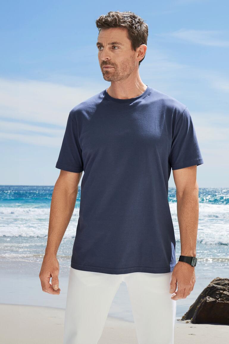 Mann in dunkelblauem T-Shirt steht am Strand mit Blick zur Kamera.